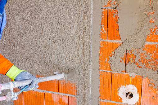 Artesano sostiene manguera de mortero para enlucir paredes en interiores de edificios residenciales sin terminar photo