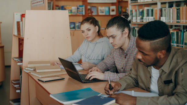 istock Focus on hipster male student in glasses using laptop computer while preparing for exams in university library with his classmates 1434617270
