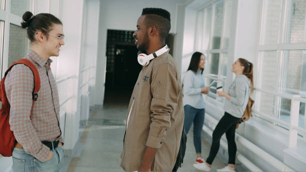 istock Caucasian and african american male students talking while standing in university hall, two girls chatting near 1434625444