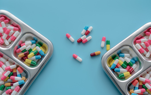 Multi-colored antibiotic capsule pill on tray and blue background. Antibiotic drug resistance and overuse. Prescription drugs. Pharmaceutical industry. Superbug problems. Medicament and pharmacology.