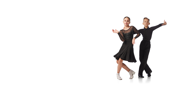 Junior dancers. Two kids, school age girl and boy in black stage costumes dancing ballroom dance isolated on white background. Art, sport dance, music, studying. Copy space for ad