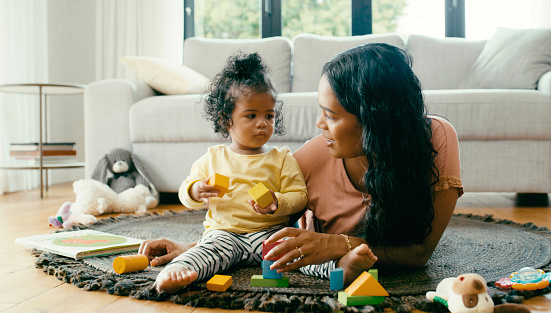 Learning, building and mother and baby on a carpet, playing, relax and bonding on a floor together. Family, child development and girl enjoy fun game with color blocks and happy parent in living room