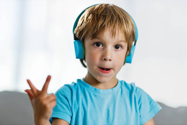 Little boy with headphones talking while having video call at home and looking at camera.