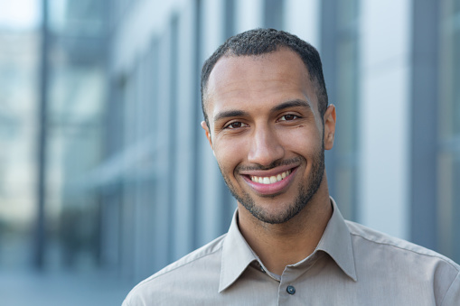 Close up photo portrait of young African American student, man smiling and looking at camera, businessman outside office building wearing shirt.