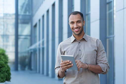 Retrato de un hombre de negocios feliz fuera de un edificio de oficinas, un hombre con una camisa informal está mirando a la cámara y sonriendo, un hombre de negocios está usando una tableta photo