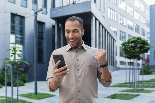 istock Successful african american businessman outside office building using smartphone, smiling and happy celebrating victory online games, got good news. 1434640628