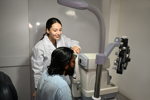 Ophthalmologist using special medical device with high precision for examination eye of patient to determine condition of lens, cornea.