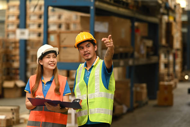 istock Two warehouse workers in hardhat and reflective jacket standing between rows of tall shelves at retail warehouse. 1434644889