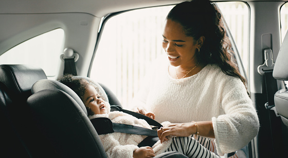 Mother, baby and car seat safety in a car before driving together, bonding while checking belt and smiling. Travel, parent and safety belt with girl relaxing before a road trip with a cheerful mom