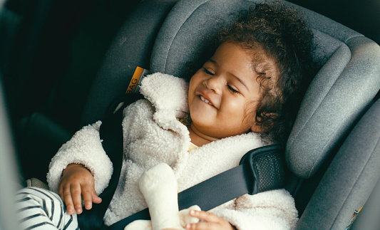 Happy, smile and girl baby in a car seat for security and safety while on a drive in a car. Happiness, travel and child or toddler sitting in a infant seat for protection in transport on a journey.