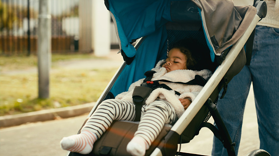 Baby, sleeping and mother walking with a stroller in the city street for care, calm or peace together in the morning. Child, kid or parent on a walk in the road with a carriage for sleep and wellness