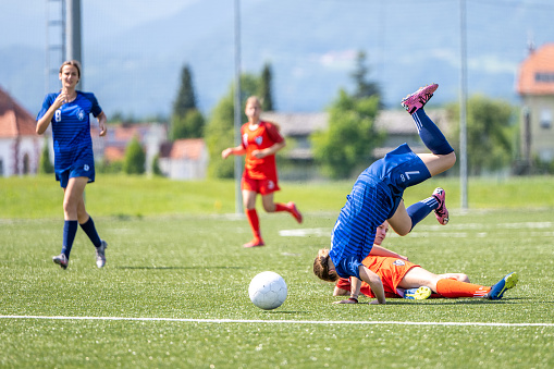 Female football players falling after being tripped by opponent during match.