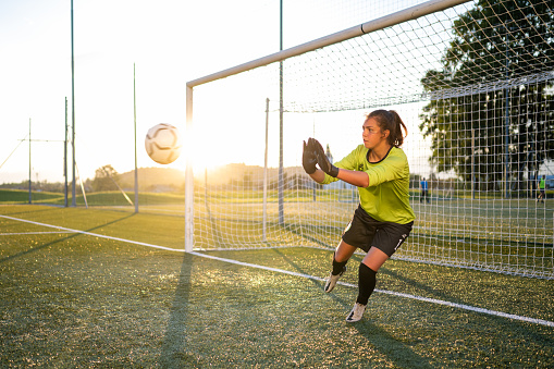 Female football player goalkeeper jumping to catch football during match.