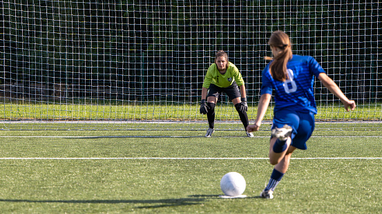 Female football player kicking ball while opponent goalkeeper looking ball during match.