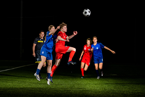 Female football players jumping and heading ball during match.