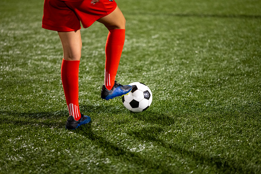 Low section of female football player with ball at soccer field.
