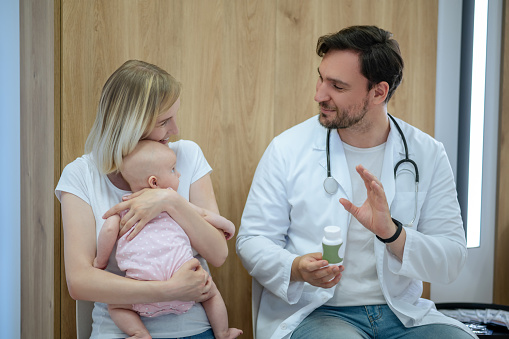 Caring young mother holding her newborn child while discussing dietary supplements with the professional pediatrician