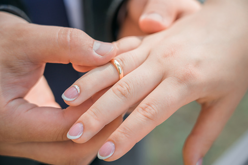 Newlyweds put wedding rings on their finger. Close-up.