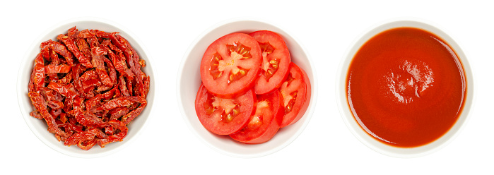 Fresh and sun-dried tomato slices, and tomato puree, in white bowls, isolated, from above.Pile of sliced, red and ripe plum tomatoes, Julienne strips of sun-dried tomatoes, and canned passed tomatoes.