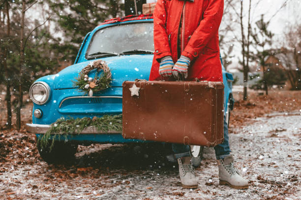 carte de vœux de noël. maquette sur une vieille valise dans les mains d’un manteau rouge de femme. voiture rétro bleu décoré couronne de noël conifères. - suitcase retro revival women old fashioned photos et images de collection