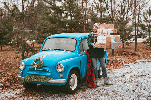 young woman preparing holiday xmas gifts Decorated with blue retro car with festive Christmas tree branches, gift boxes craft wrapping paper, New Year trip. dream, memories desires.
