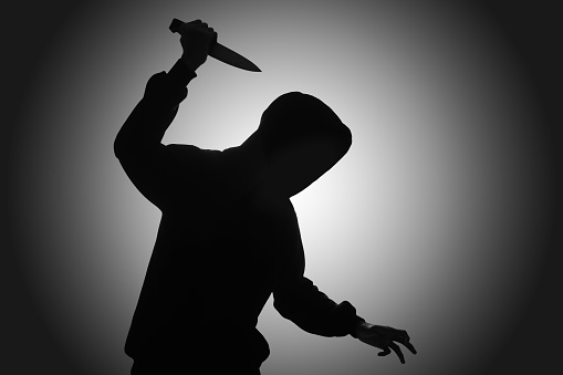 Mysterious man wearing black hoodie holding a knife to stab someone. Crimes and criminality concept