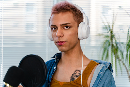 transgender person with microphone is recording podcast at home or studio