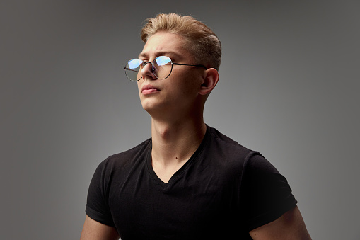 Portrait of young stylish man with blonde hair posing in black casual T-shirt isolated over grey studio background. Fahsion trends. Concept of men's health, natural beauty, body and skin care.