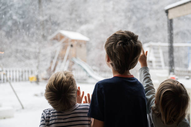 View from behind of three children, siblings, looking out the window into a beautiful winter nature stock photo