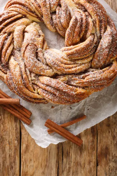 Estonian Kringle Cinnamon Braid Bread with powdered sugar closeup on the paper on the wooden table. Vertical top view from above