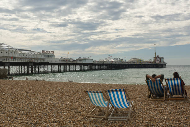 Brighton beach and pier, England Shingle beach with people in deckchairs and pier at Brighton in East Sussex, England brighton england stock pictures, royalty-free photos & images