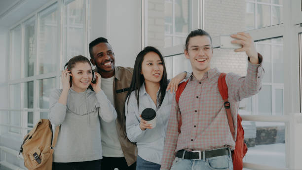 istock Group of multi-ethnic students taking selfie on smartphone camera while standing in corridor of university . Hipster guy holding phone and friends are posing positively 1434681757
