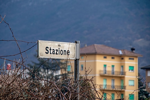 Rusty Via Stazione sign near bushes and a building in Italy