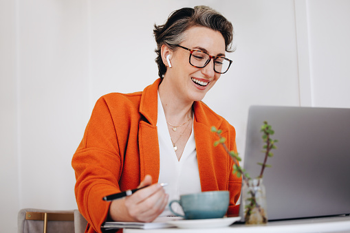 Smiling business woman attending a virtual meeting while working in a cafe. Happy mature businesswoman having a video call with her team while working remotely.