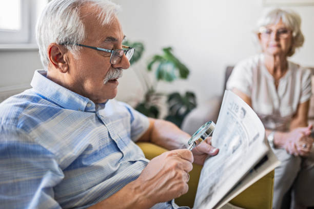 senior man holding an magnifying glass he uses to help him read - macular degeneration imagens e fotografias de stock