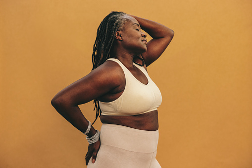 Athletic woman standing against a studio background with her eyes closed. Mature woman with dreadlocks wearing sports clothing in a studio. Sporty black woman maintaining a healthy lifestyle.