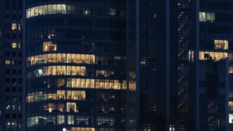 Time lapse day to night transition blinking office windows lights in business center building downtown. Corporate business, high skyscraper glass surface. Light in building windows turn on and off