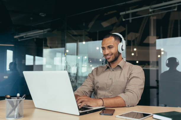 jovem funcionário de escritório trabalhando dentro do prédio do escritório, usando laptop para assistir vídeo e fones de ouvido, empresário no intervalo - new life audio - fotografias e filmes do acervo