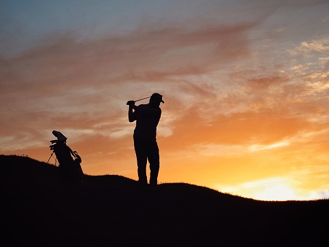 Silhouette of golfer, mid swing at sunset