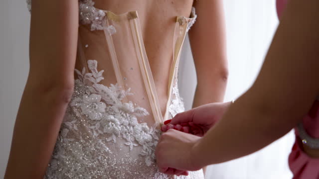 Unrecognizable woman helping bride, to dress into a wedding dress