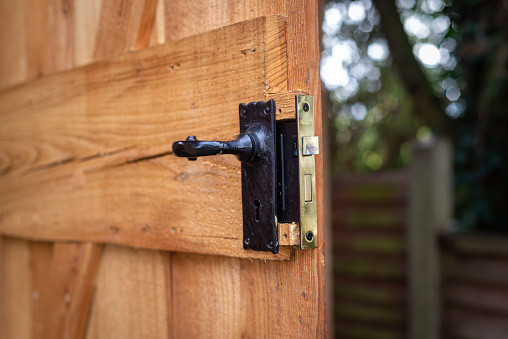 Close up of black metal door handle with mortise lock on open wooden shed door in residential garden.