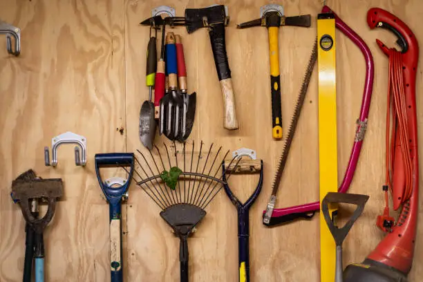 Photo of Assortment of DIY gardening tools and equipment hanging organised on wooden wall inside garden shed.