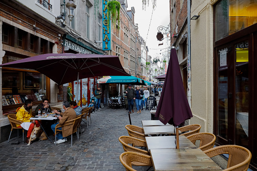 Brussels, Belgium - September 18, 2022: Sidewalk cafes along a narrow cobbled street leads between buildings in the old town. People are there.