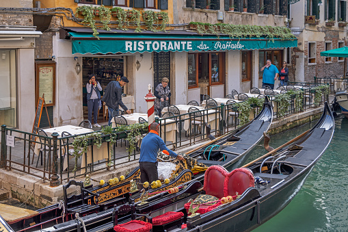 Venice, Italy - October 6th 2022: Man in a gondola trying to get customers from a outdoor restaurant in the center of Venice