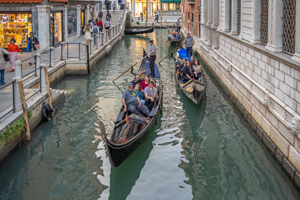 Venice, Italy - October 5th 2022: Gondola heavy loaded with tourists sailing down a narrow canal on a late afternoon