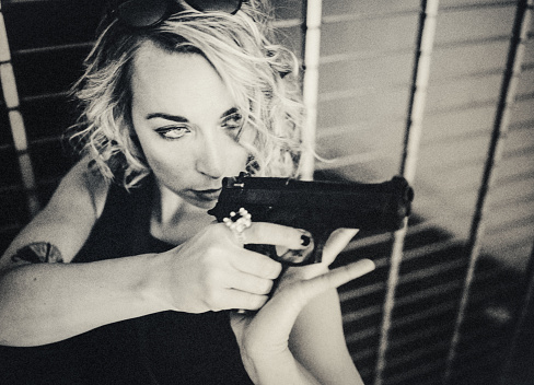 Portrait of a young woman with a pistol. It is the moment of deciding. She has just jerked the gun up. Dark and mysterious, Film Noir style.