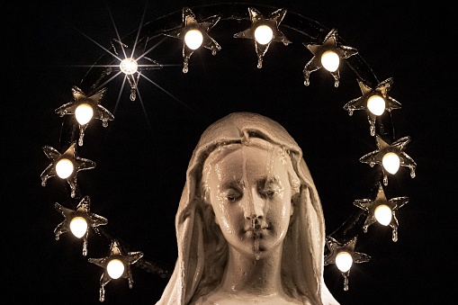 A closeup of the statue of Virgin Mary surrounded with stars on a black background.