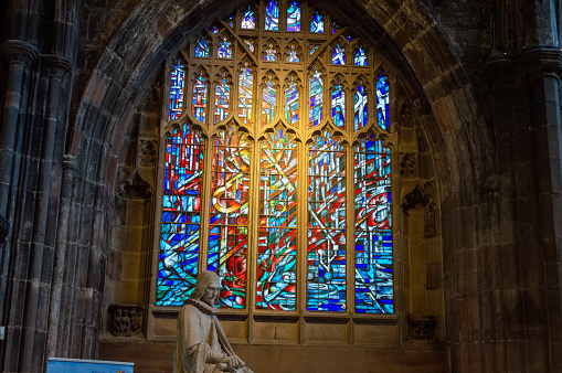 A stained glass window in Manchester Cathedral with a statue in front of it