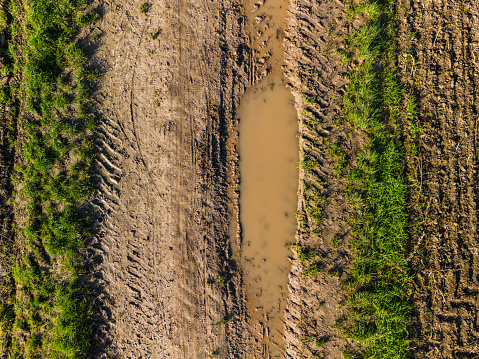 Tracks between puddles of water and grass on a dirt road after the rain seen from above