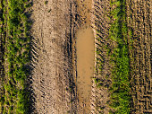istock Tracks between puddles of water and grass on a dirt road after the rain seen from above 1434708612